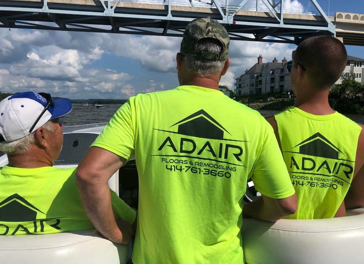 Three generations of the Adair family together on a boat on a Wisconsin lake, all wearing Adair Floors & Remodeling shirts.